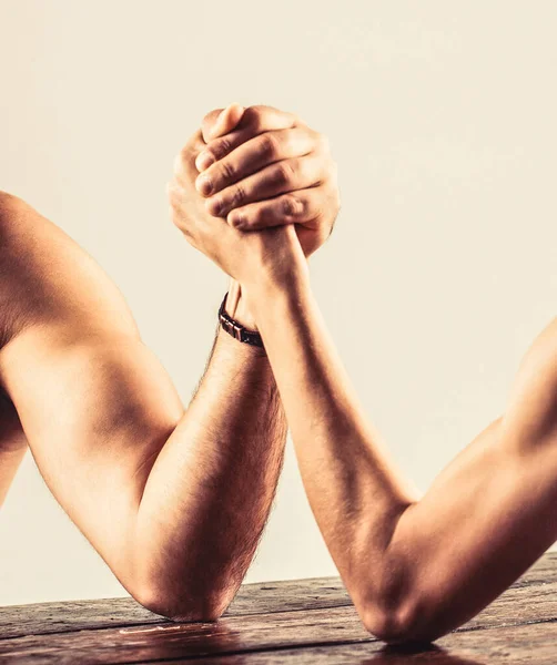 Two mans hands clasped arm wrestling, strong and weak, unequal match. Arm wrestling. Heavily muscled bearded man arm wrestling a puny weak man Stock Photo