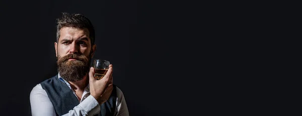 Un homme barbu tient du cognac de verre. Boire du cognac barbu. Un homme tenant un verre de whisky. Siroter du whisky. Portrait d'homme à la barbe épaisse. Macho potable — Photo