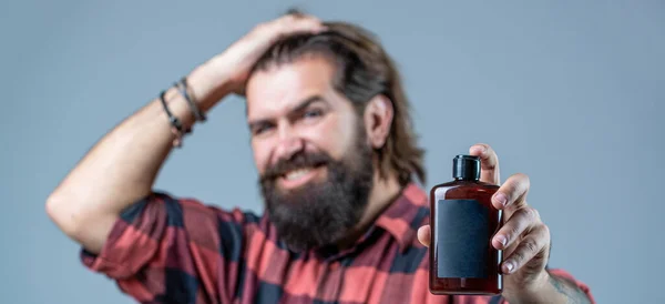 Champú acondicionador para hombres. Cuidado experto para el cabello exigente. Envase de plástico con champú. Joven hombre guapo aplicando crema de loción. Hombre sostiene botella negra de champú o gel de ducha —  Fotos de Stock