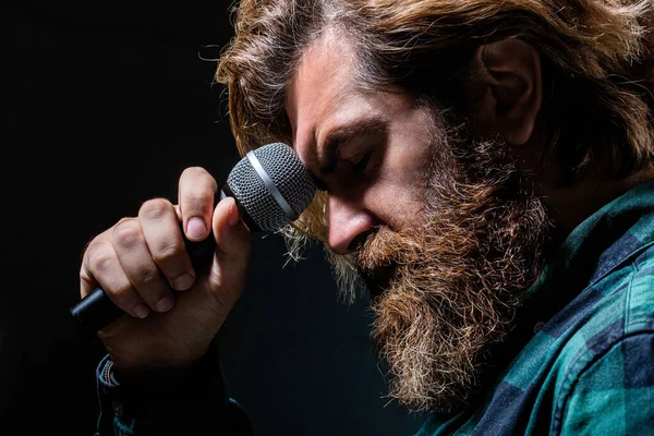 Male singing with a microphones. Man with a beard holding a microphone and singing. Bearded man in karaoke sings a song into a microphone. Male attends karaoke. Bearded man singing with microphone — Stock Photo, Image