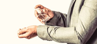 Resmi takım elbiseli yakışıklı bir adam ve bir şişe parfümlü, yakın plan. Elinde parfüm şişesi tutan bir adam. Erkek parfümü, takım elbise arka planında