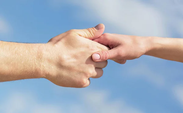 Giving a helping hand. Hands of man and woman on blue sky background. Lending a helping hand. Hands of man and woman reaching to each other, support. Solidarity, compassion, and charity, rescue