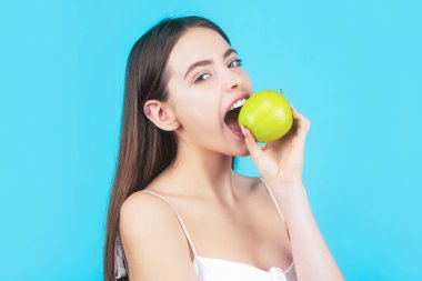 Kadın yeşil elma yiyor. Yeşil elmalı güzel ve mutlu bir kadının portresi. Sağlıklı diyet yemekleri. Stomatoloji konsepti. Mükemmel gülüşü olan, elma tutan, mavi arka planlı bir kadın.