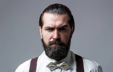 Beyaz gömlek, papyon ve pantolon askısı takmış sakallı yakışıklı bir adamın portresi. Bir beyefendinin papyonuna yakın çekim. Papyonlu ve askılı sakallı adam. Renkli kravatını düzelten gömlekli bir erkek.