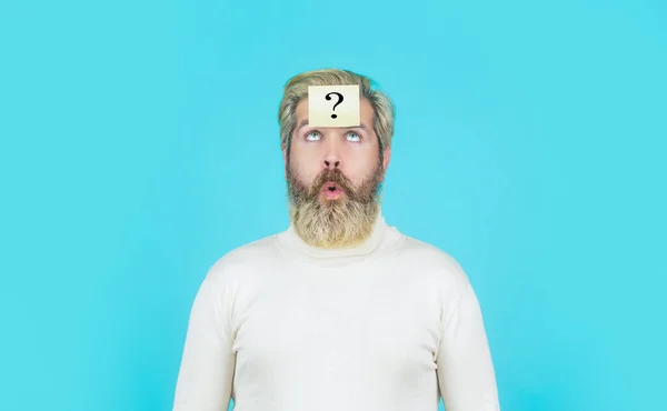 Thinking man with question mark on blue background. Man with question mark on forehead looking up. Paper notes with question marks. Beard man question mark in head, solution problems