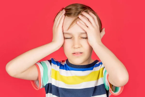 Retrato de un niño triste sosteniendo la cabeza con la mano, aislado sobre el fondo rojo. Un niño con dolor de cabeza. Desesperación, tragedia —  Fotos de Stock