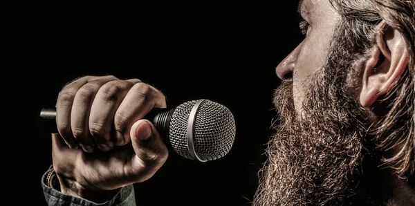 Bearded man in karaoke sings a song into a microphone. Male attends karaoke. Male singing with a microphones. Man with a beard holding a microphone and singing — Stock Photo, Image