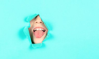 Çocuk dilini duvardaki delikten gösteriyor. Yırtık bir kağıtta dilini gösteren komik çocuk portresi. Yakından Erkek Surat Dilini Gösteriyor. Çocuk dilini kağıttaki bir delikten çıkarmış.