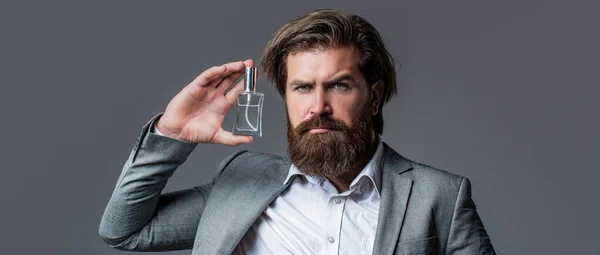 Man perfume, fragrance. Perfume or cologne bottle and perfumery, cosmetics, scent cologne bottle, male holding cologne. Masculine perfume, bearded man in a suit. Male holding up bottle of perfume