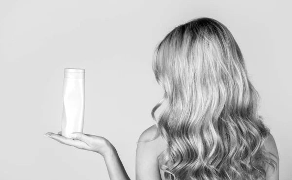 Γυναίκα κρατάει μπουκάλι σαμπουάν. Όμορφη ξανθιά με ένα μπουκάλι σαμπουάν στα χέρια. Κορίτσι με λαμπερά και μακριά μαλλιά. Γυναικεία μακριά μαλλιά. Μαύρο και άσπρο — Φωτογραφία Αρχείου