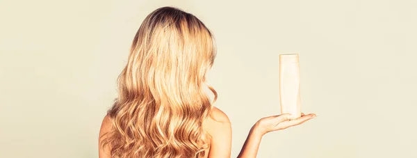 Mujer sosteniendo una botella de champú. Hermosa chica rubia con una botella de champús en las manos. Chica con el pelo brillante y largo. Pelo largo de mujer. Copiar espacio — Foto de Stock