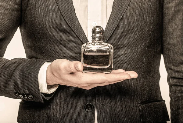 Man in a suit holding a bottle of perfume isolated on white background. Perfume or cologne bottle and perfumery, cosmetics, scent cologne bottle, male holding cologne. Male holding up bottle perfume — Stock Photo, Image