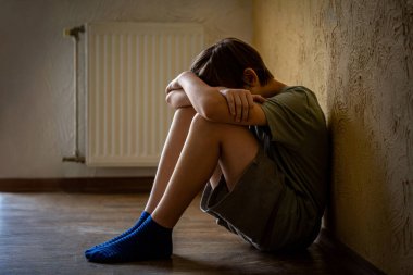 Çocuk bağırıyor, elleriyle yüzünü kapatıyor, zorbalık yapıyor. Yalnız bir çocuk odada oturur. Evde tek başına oturan üzgün çocuk depresyondan muzdarip. Korkmuş küçük çocuk yüzünü kapatıyor..