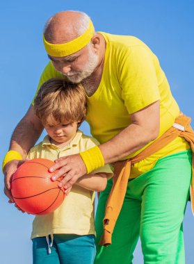 Büyükbaba ve torunu basketbol oynayıp eğleniyorlar. Çocuklar basketbol oynarken spor öğretmenlerine gülümsüyorlar..
