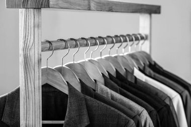 Perakende giyim mağazasında askıda asılı farklı renklerde erkek giysileri, yakın plan. Siyah ve beyaz.