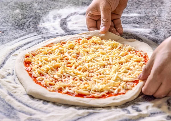 Pizza, peynir. Masada pizzaya peynir ekleyen adam, yakın plan. Yemek pişirme konsepti - Pizzacıda pizzamya rendelenmiş peynir eklemek.