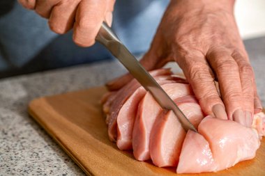 Şef eller tavuk filetosunu bıçakla kesti. Tavuk kesme teknolojisi. Erkek elleri ahşap tahtada tavuk filetosu kesiyor, masa, yakın plan. O kadın mutfakta tavuk kesiyor..