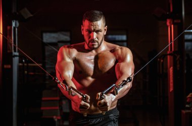 Beden dersinde kesiştim. Spor salonunda kaslı yakışıklı bir adam. Spor salonundaki makine. Fitness adamı egzersiz kablosu ile çalıştırır.