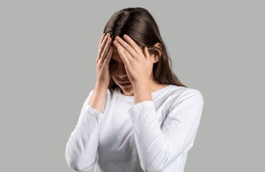 Kadın, gri arka planda, stres hissederek şakaklarına dokunuyor. Baş ağrısı çeken bir kız. Soğuk belirtileri. Baş ağrısı çeken kadın çaresiz, acı ve migren yüzünden stresli..