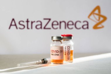Bükreş, ROMANIA - 10 Şubat 2021: Yeni Coronavirus COVID-19 aşısı dozuyla birlikte arka planda AstraZeneca logosu bulunan illüstrasyon konsepti resmi.