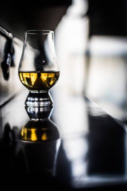 Renkli yakın çekim, bir el Glencairn viski bardağını ahşap bir masada sığ bir tarla derinliğinde tutuyor..