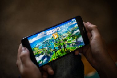 Bükreş, ROMANIA - 10 Mayıs 2021: Cep telefonuyla Fortnite oyunu oynayan bir çocuğun illüstrasyon konsepti. Fortnite, Epic Games tarafından oynanan çok oyunculu Battle Royale oyunudur.. 