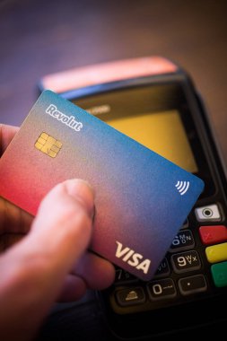 Bükreş, ROMANIA - 17 Mayıs 2021: POS terminali yakınlarında Revolut VISA kartı tutan kişinin resimli editörlük konsepti. 