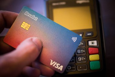 Bükreş, ROMANIA - 17 Mayıs 2021: POS terminali yakınlarında Revolut VISA kartı tutan kişinin resimli editörlük konsepti. 