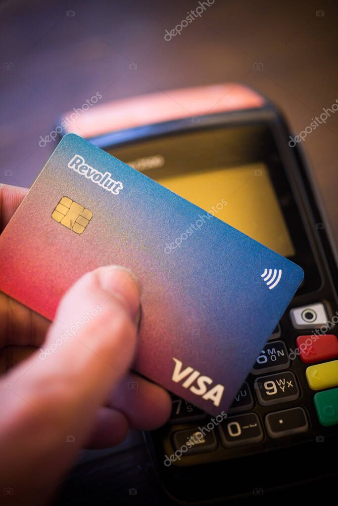 Bucharest, ROMANIA - May 17, 2021: Illustrative editorial concept image of a person holding a Revolut VISA card near a POS terminal.