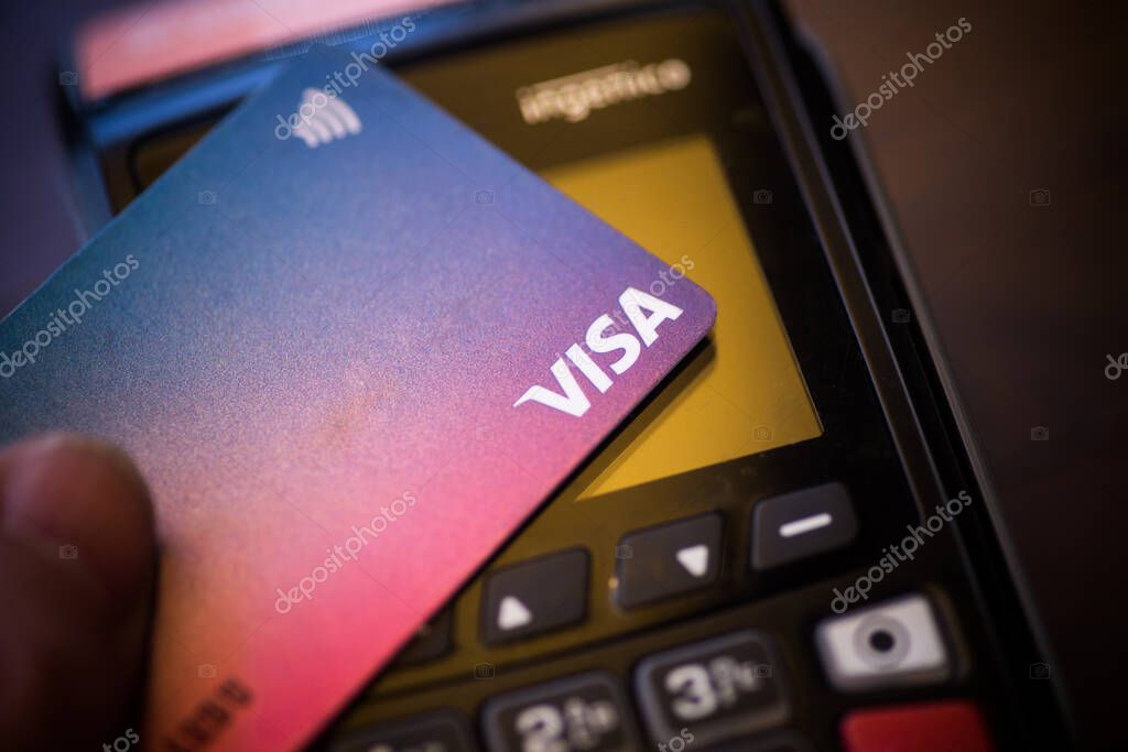 Bucharest, ROMANIA - May 17, 2021: Illustrative editorial concept image of a person holding a VISA card near a POS terminal.