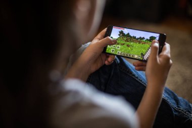 Bükreş, ROMANIA - 10 Mayıs 2021: Cep telefonuyla Minecraft oyunu oynayan bir çocuğun resimli editör konsepti.
