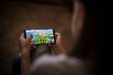 Bükreş, ROMANIA - 10 Mayıs 2021: Cep telefonuyla Fortnite oyunu oynayan bir çocuğun illüstrasyon konsepti. Fortnite, Epic Games tarafından oynanan çok oyunculu Battle Royale oyunudur.. 