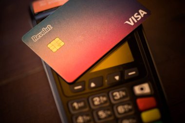 Bükreş, ROMANIA - 17 Mayıs 2021: POS terminali yakınlarında Revolut VISA kartı tutan kişinin resimli editörlük konsepti. 