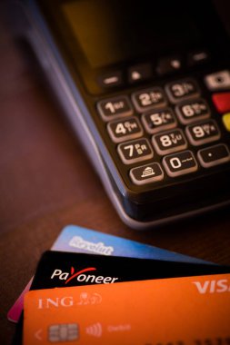 Bükreş, ROMANIA - 17 Mayıs 2021: POS terminali yakınlarında bir Revolut, ING ve Payonez kartı tutan kişinin resimli editörlük konsepti. 