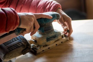 Elektrikli kum makinesi kullanarak tahta zımparalayan adam..