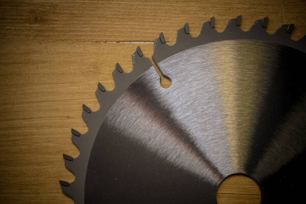 Color detail of a new circular saw blade on a wooden background.