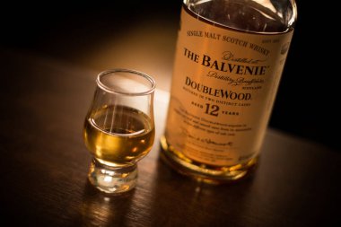 Bükreş, Romanya - 5 Ağustos 2021: Bir barda tezgahın üzerinde duran bir bardağın yanında tek bir malt Balvenie viski şişesinin resimli editörlük resmi.