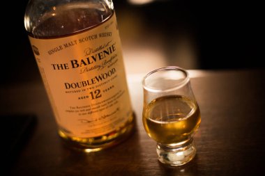Bükreş, Romanya - 5 Ağustos 2021: Bir barda tezgahın üzerinde duran bir bardağın yanında tek bir malt Balvenie viski şişesinin resimli editörlük resmi.
