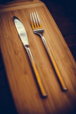 Ahşap bir masanın üzerinde parlak bir bıçak ve çatal..