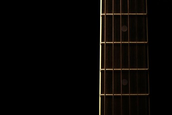Detail of the fret board of an acoustic guitar, on a dark background.