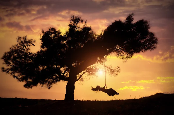 Silhueta de feliz jovem mulher em um balanço com o pôr do sol fundo — Fotografia de Stock