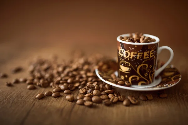 Copo cheio de grãos de café no fundo de madeira — Fotografia de Stock
