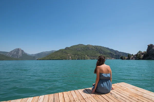 Junge Frau sitzt auf Seebrücke und genießt den Blick auf den See — Stockfoto