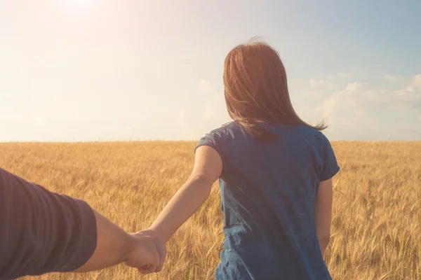 Young woman holding man hand on the wheat field — Stock fotografie