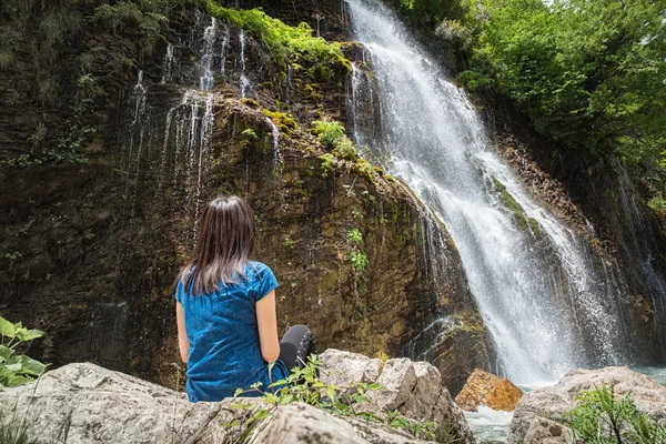 Junge Frau sitzt und schaut auf den Wasserfall — Stockfoto
