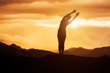 Gün batımında yoga yapan genç bir kadın.