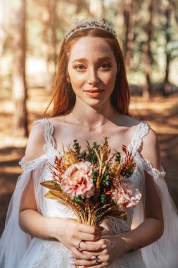 Ormanda beyaz gelinlikli gelin elinde renkli ve kuru bir düğün buketi tutuyor.. 
