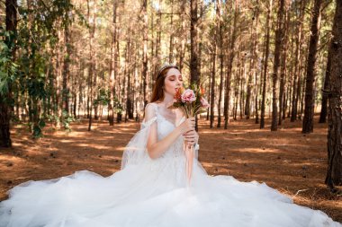 Ormanda beyaz gelinlikli gelin elinde renkli ve kuru bir düğün buketi tutuyor.. 