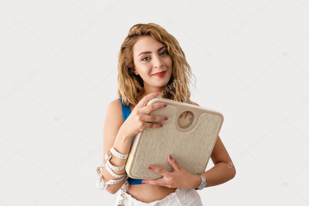 Young beautiful woman is holding for a tape measure and a scale for measuring her waist and check her weight for a healthy life and fit body