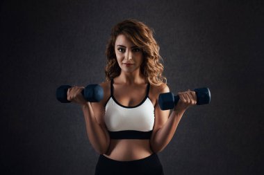 Güzel bir kadın, sağlıklı bir yaşam için dambılları kaldırıyor.